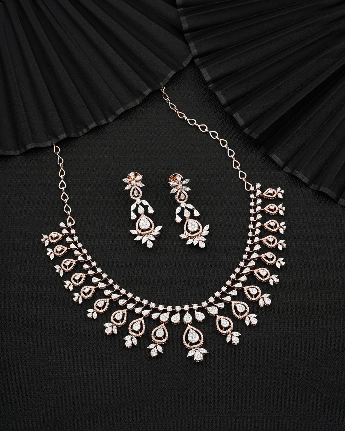 Modern rose gold diamond necklace and earrings on black fabric